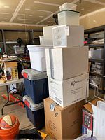 Wide shot showing stacked plastic totes of various sizes, cardboard boxes labeled scrapbook supplies and men's shoes, and smaller plastic organizers on top.