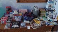 Overview of the lot showing space heater, toiletries, scarves, gloves, and Space Bags on a wooden table