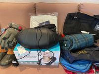 Overview of all lot contents on couch: gloves, boots, massager on box, assorted bags