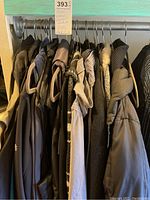 Photo of multiple women's coats and jackets hanging on a rod, colors mostly dark and neutral, varying materials.