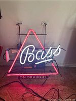 Full view of the neon sign showing the red triangular frame with 'Bass' in white neon script inside, and 'On Draught' on a panel beneath.