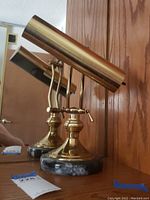 Brass desk lamp showing polished cylindrical shade, curved arm, and black marble base.