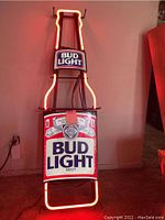 Full view of Bud Light neon sign in the shape of a beer bottle with red neon illumination and logo panels.