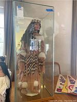 Front view of the doll standing inside a rectangular glass and wooden display case.