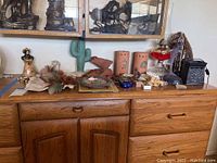 Wide shot of wooden dresser with various Native American southwestern decorative items arranged on top, including pottery, figurines, lamp, feathers, and artwork.