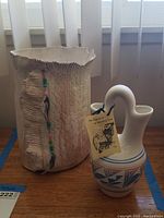 Photo showing two items on a wooden surface by a window: a Native American wedding vase with story tag and a textured decorative vase resembling leather with bead embellishments.