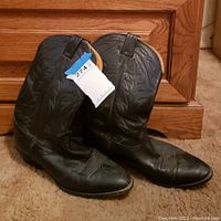 Side view of Nocona black leather cowboy boots showing decorative stitching and pull tabs with a blue tag attached.