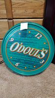 Front view of round green Odoul's bar lamp electric sign with logo and clock numbers on carpeted floor.