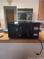 Front view of a black Oster microwave oven with visible control panel and power cord.