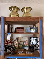 Wide view of wooden shelving unit holding various lot items including brass scales, Route 66 signs, Native American art, goggles, metal scale and wooden box.
