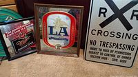 Photo showing the Miller Genuine Draft mirrored sign, LA Busch mirrored sign in frames, and metal Railroad Crossing sign on carpeted floor.