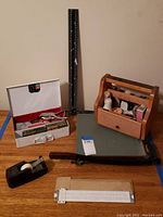 Photo showing entire lot from above, including wooden shoe shine box, metal box with tools, paper cutter, tape dispenser, clipboard, and ruler