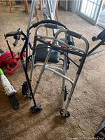 View of two walkers and a red cane arranged close together on carpeted floor, showing padded seat on one walker and handles on the other walker.
