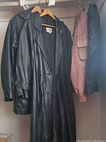 Four leather coats on hangers including two long black leather coats, one black mixed fabric and leather zippered jacket, and one brown leather jacket with quilted shoulder detail.