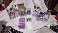 Eight Precious Moments figurines with most in lavender and white boxes, with one blue mug visible. All figurines depict children in pajamas or cute poses, mostly unboxed but some in boxes.