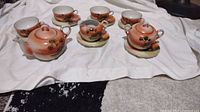 Full set including two lidded pieces, creamer, 5 cups, 5 saucers on white cloth.