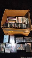Full box of cassette tapes, some cassettes and cases laid out in front, showing condition and variety.