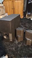 Three Bose SE5 speakers arranged on black carpet showing subwoofer and smaller satellites with wiring tangled nearby.