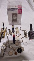 Overview photo including 13 watches and several loose watch parts arranged on a white cloth.