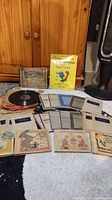 Photo of the entire lot showing vintage records, sheets, and children's books spread on floor with a wooden cupboard background.
