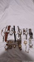 Overview of all 14 watches laid out on white fabric, showing mix of metal and leather bands and various face shapes.
