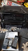 Kenwood KR-V7030 stereo receiver stacked with DPM6630 CD player on top, three remote controls placed nearby, and instruction manual partially visible.
