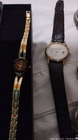 Close-up of two wristwatches; left gold-tone Le Grand with black dial, right Boeing watch with black leather strap and white dial featuring a small airplane logo