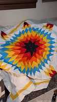 Full view of the folded quilt showing the vibrant radial geometric star pattern in red, orange, yellow, black, blue, and white.