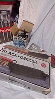 Photo showing the boxed Black+Decker electric griddle, partially opened cardboard box with kitchen tools in packaging behind.