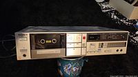 Front view of silver Sony TC-FX410R cassette player recorder with cassette loaded, showing control buttons, analog meter, headphone jacks, and power switch.