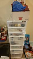 Stack of plastic storage drawers with boxes and bags on top, containing various craft materials inside drawers