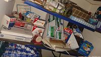 Photo showing assorted medical supplies including boxes of bandages, adhesive tapes, and cold packs on shelving.