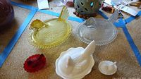 Five Fenton chicken on a nest glass bowls in yellow, clear, white milk glass, and red glass on carpeted floor.