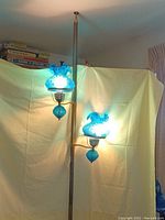 Full view of the pole lamp with two blue art glass shades lit up, showing overall height and design.