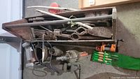 Overview of lot showing assorted long handled hand tools, electric grinder, pick axe heads, vise and chisels.
