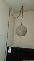 Hanging swag lamp suspended by a long chain with textured spherical shade near a wall and ceiling corner.