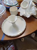 Milk glass scalloped edge plate and a matching milk glass flower vase or candle holder on a wooden table
