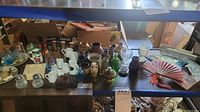 Table with assorted miniature bowls, ceramic and glass vases, mini mugs, and salt and pepper shakers arranged for sale, along with a decorative fan and fans.