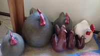 Five decorative rooster figures including three large round dark grey hens with red combs and two smaller roosters, one dark brown and one white with a red comb and yellow beak.