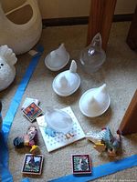 Top view of three white milk glass chicken bowls, one clear glass chicken bowl, two colorful rooster figurines, and four rooster coasters or tiles on carpet.