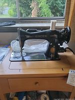 Front and side view of the black Singer sewing machine mounted on a wooden sewing table by a window.