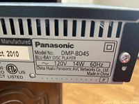 Close-up photo of label on the Panasonic Blu-ray player showing model number DMP-BD45, power specifications, manufacturing details, and certification markings.