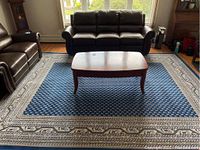 Living room scene showing 8x10 navy area rug with beige border and coffee table on top