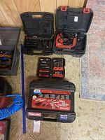 View of Arrow staple gun in orange case, Craftsman cordless screwdriver in black case, and Craftsman drill/driver bit set case on floor