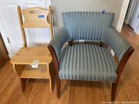 Front view of the two chairs side by side, showing the wooden chair with shelving under seat and the blue upholstered armchair