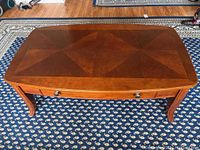 Full view of rectangular wooden coffee table with single drawer and curved legs on patterned rug.