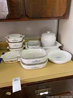 Wide view of the Corningware bakeware set including Cornflower Blue and L'Echalote patterns, white ceramic cookie jar, and various glass-lidded dishes on a kitchen counter.