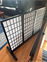 Front view of three-panel folding Shoji screen standing on hardwood floor with visible grid pattern wooden framing and white paper panels.