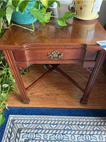 Front view of wooden end table showing drawer with ornate metal handle, visible scratches on surface, and decorative leg details.