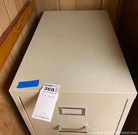 Top view of beige metal file cabinet with closed drawers and a label marked 'File Cabinet C'. Cabinet shows signs of wear and is placed against wood panel wall.